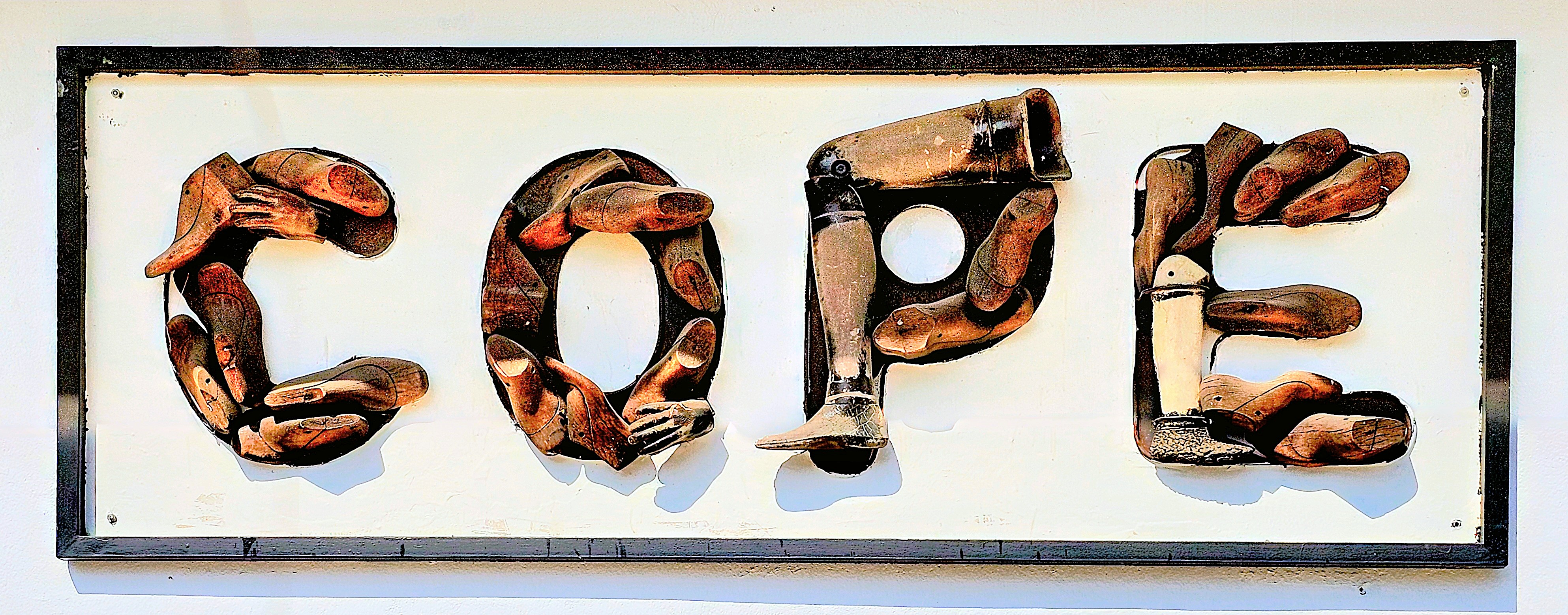 A sign made of crafted wooden elements forming the word 'COPE', representing a rehabilitation organization providing support for individuals affected by landmines and unexploded ordnance in Laos.