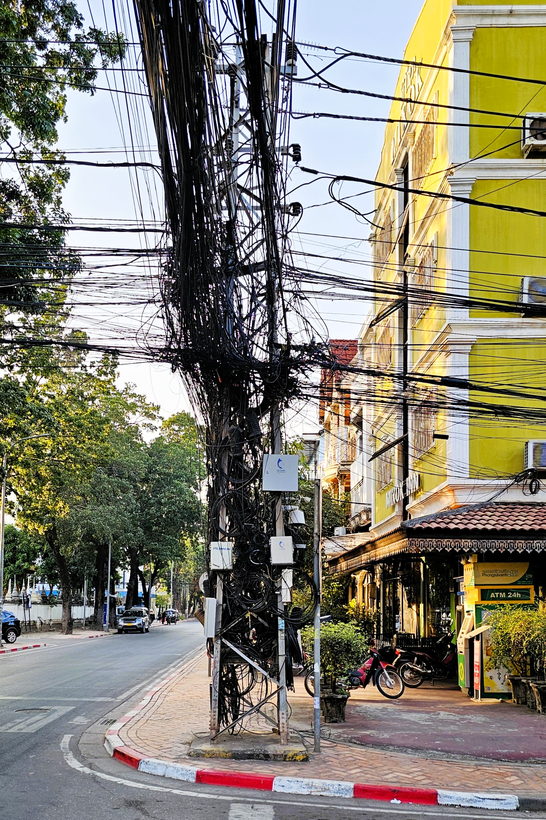 A tangled mess of electrical wires connects to a utility pole on a street in Laos, showcasing the country's infrastructure challenges.