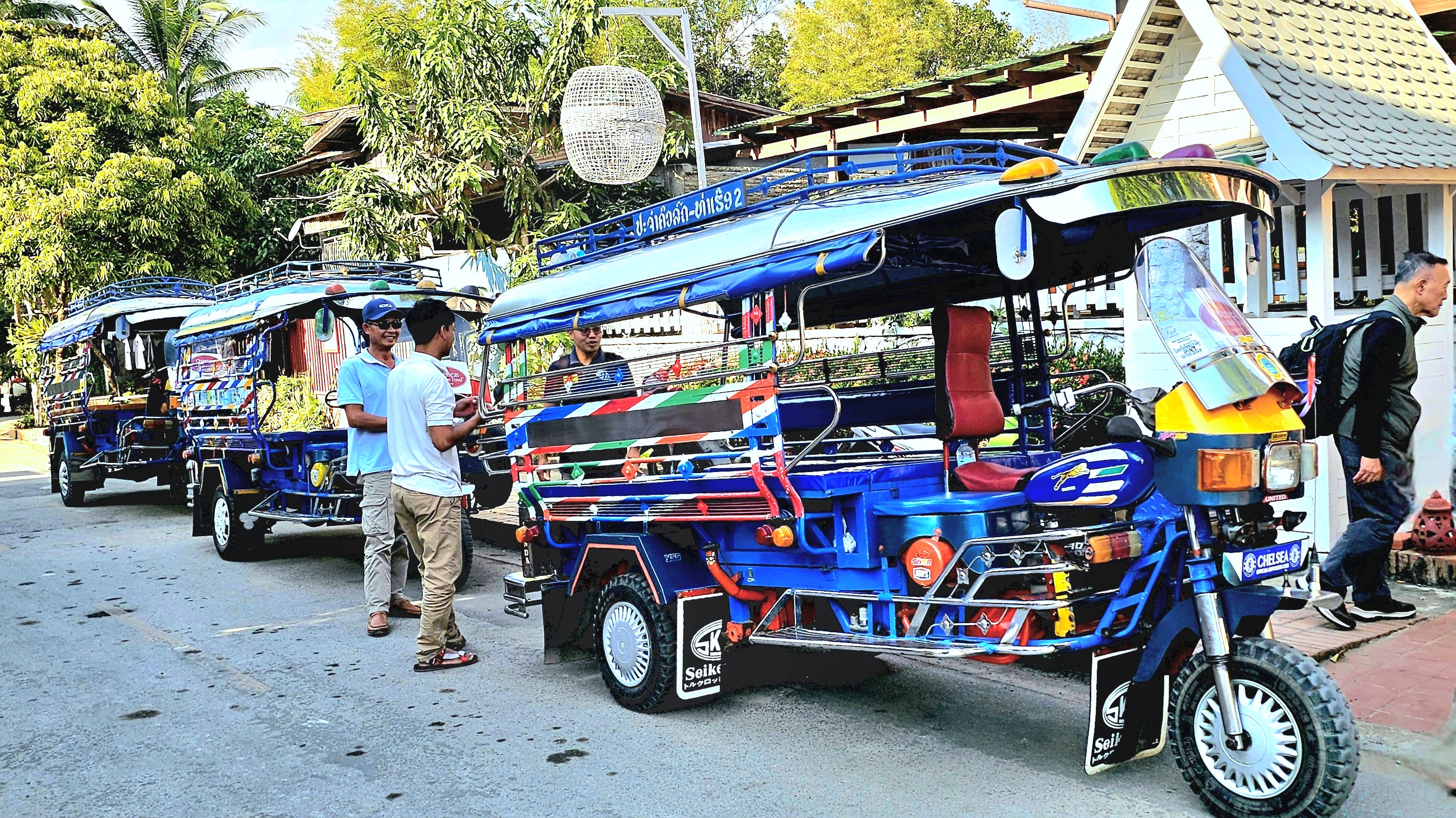 Two local men chatting near colorful shared transport vehicles in a vibrant street setting.