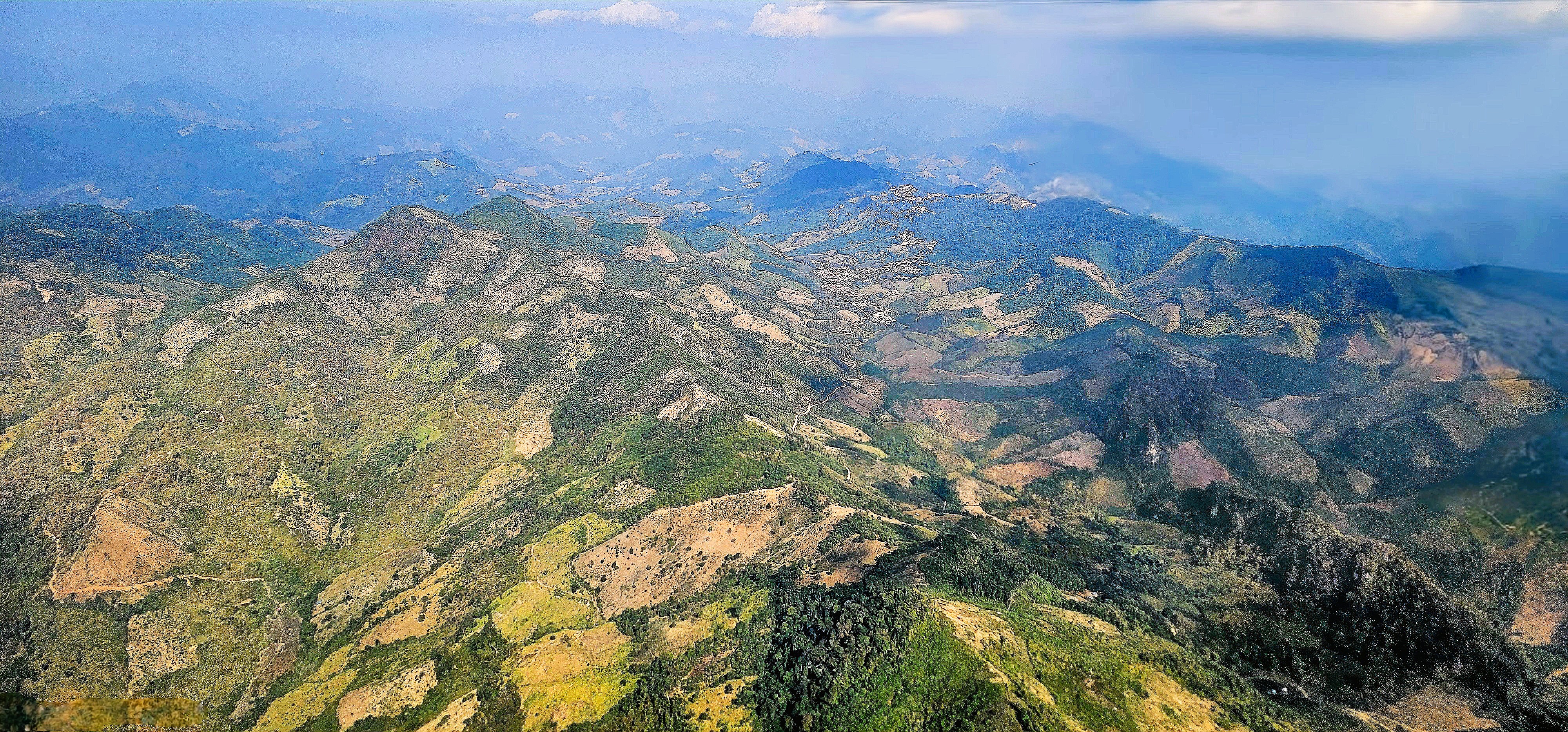 Aerial view of the mountainous terrain in Laos, showcasing a mix of greenery and cleared land.