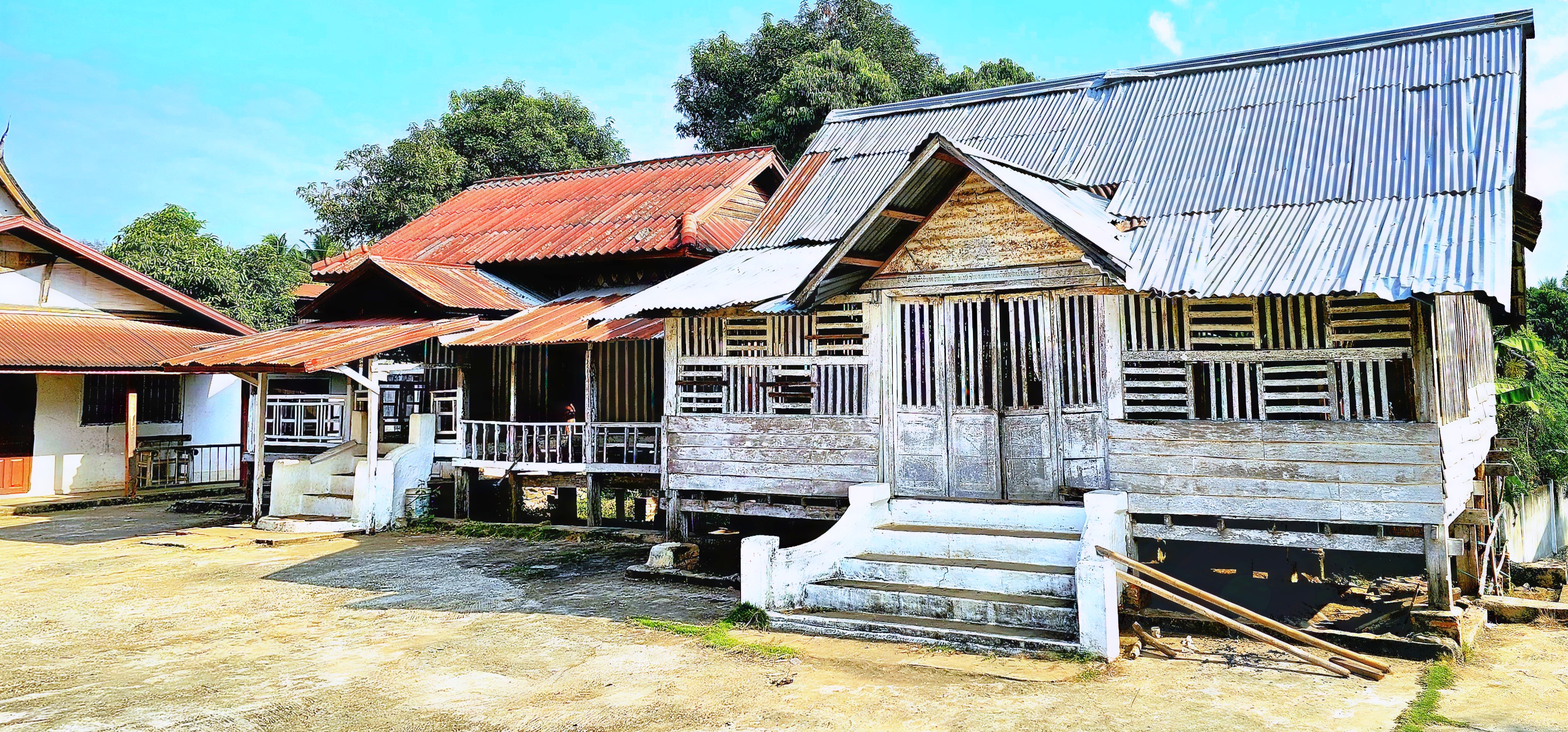 Rural wooden houses with metal roofs in a village, showcasing traditional architecture against a clear blue sky.