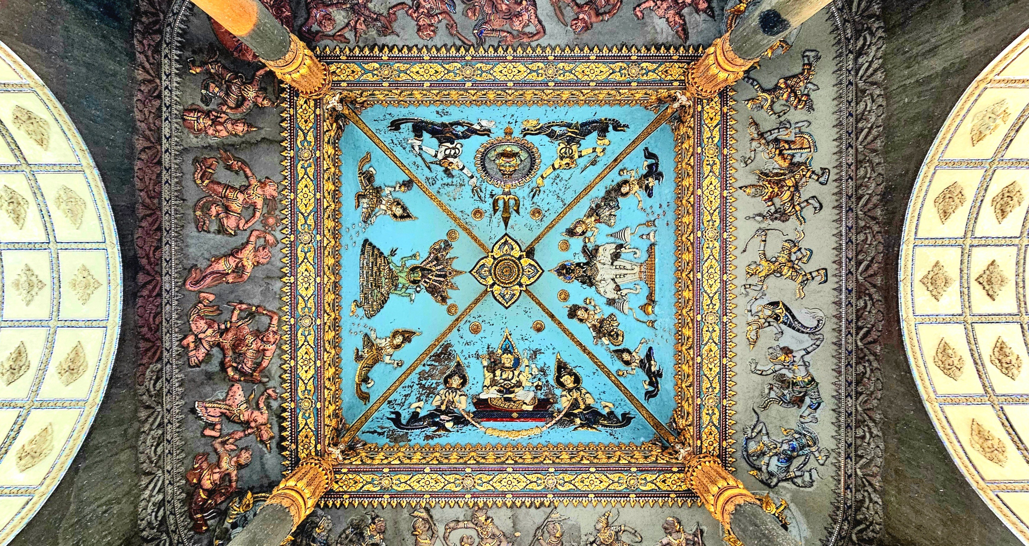 A decorative ceiling featuring intricate traditional Lao and Buddhist designs, including mythical figures and vibrant colors, showcasing the cultural heritage of Laos.