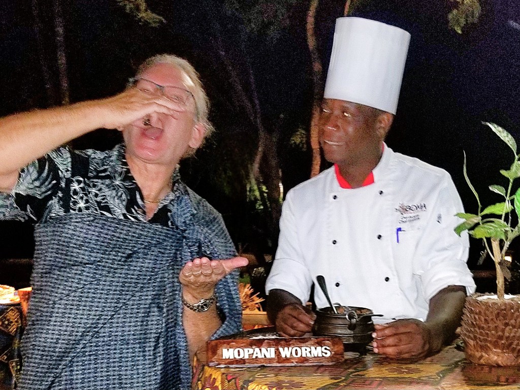 A person reacting with surprise while holding food in their hand, with a chef in a white hat smiling beside them.