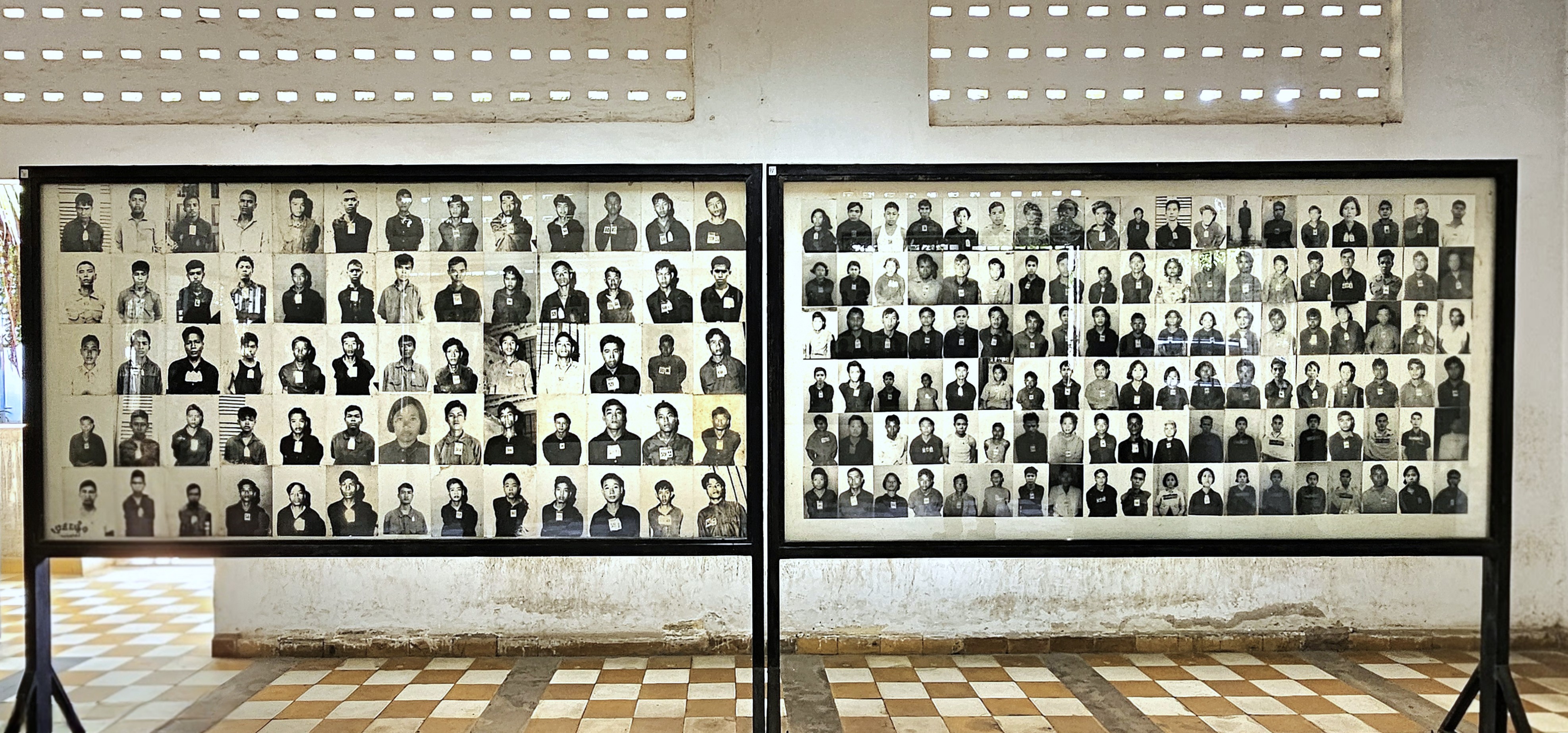Two large display frames containing black and white photographs of individuals, each wearing identification tags. The images are arranged in a grid pattern, showcasing the faces of detainees from the Khmer Rouge era.