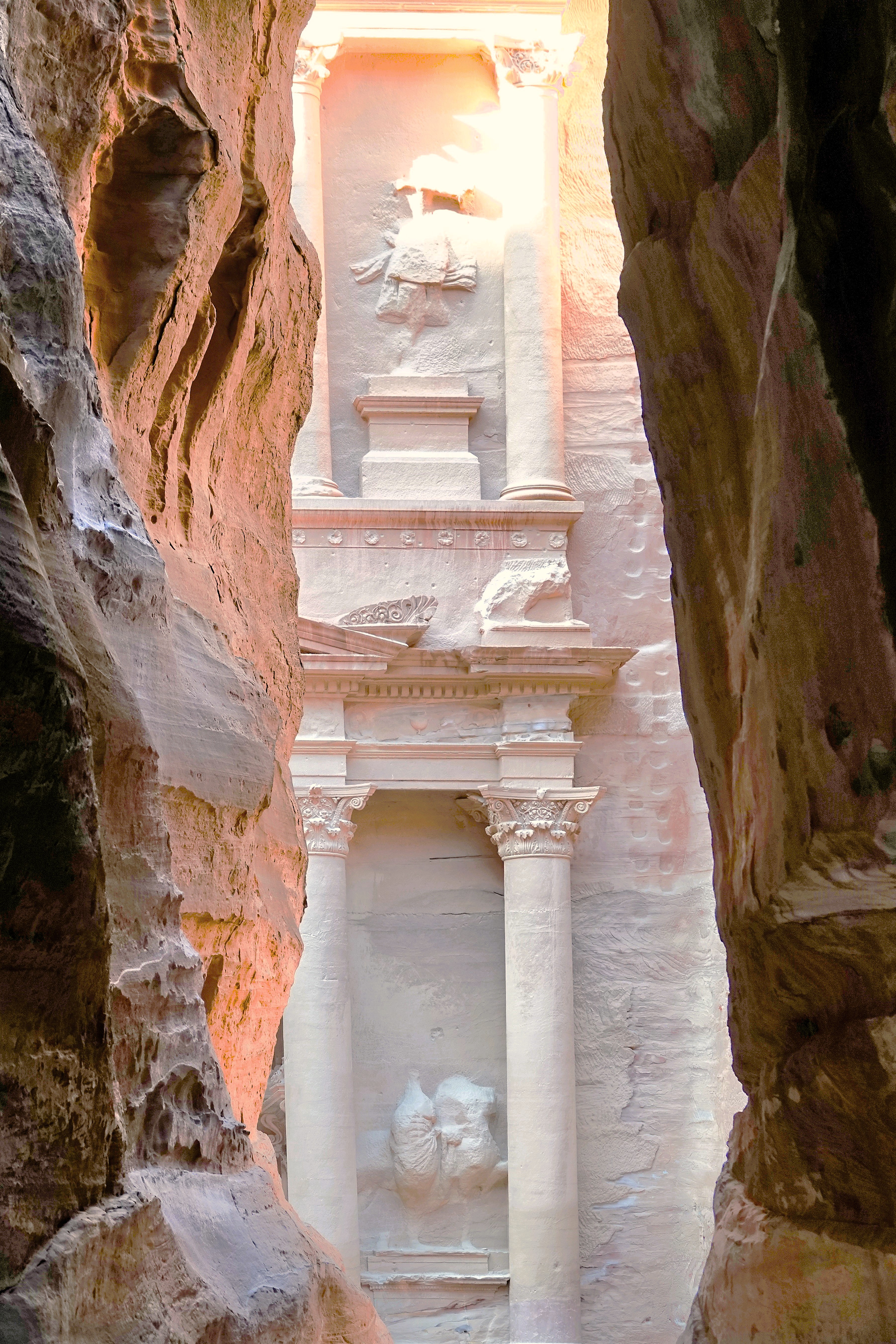 A view of the intricate architecture of Petra, framed by tall rock cliffs, showcasing carved columns and reliefs in the sandstone.