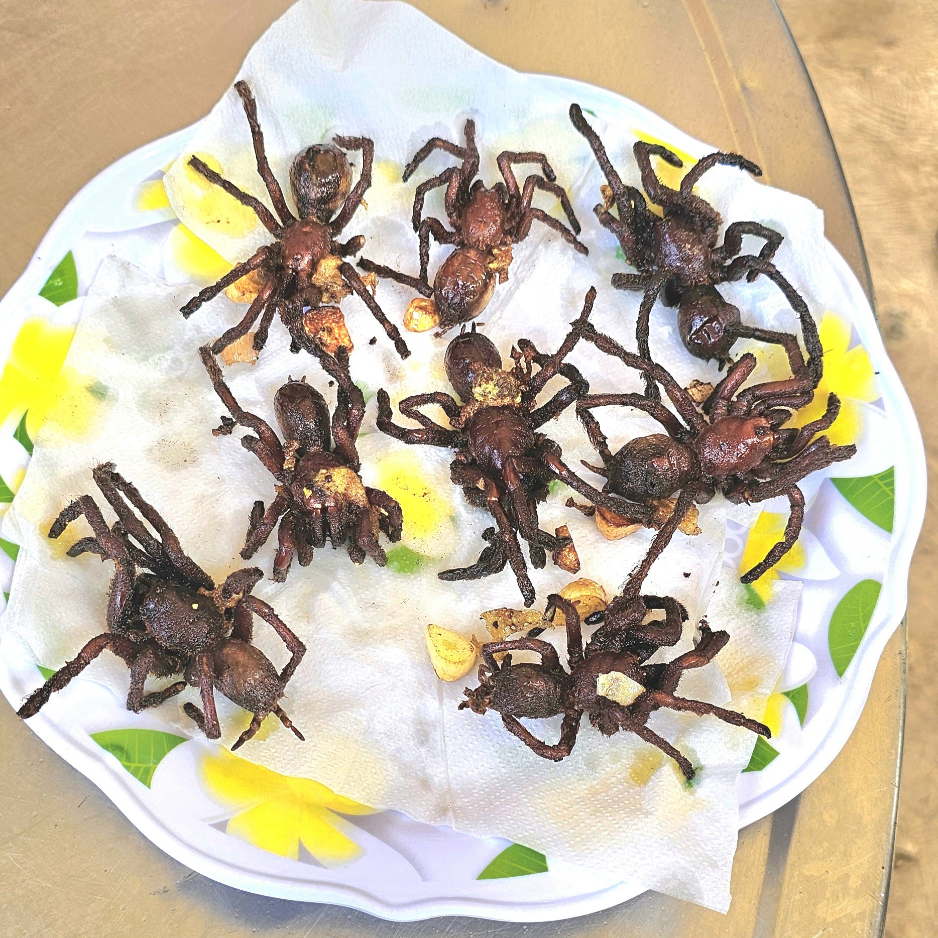 A plate of deep-fried tarantulas, served on a paper towel with a floral patterned edge.