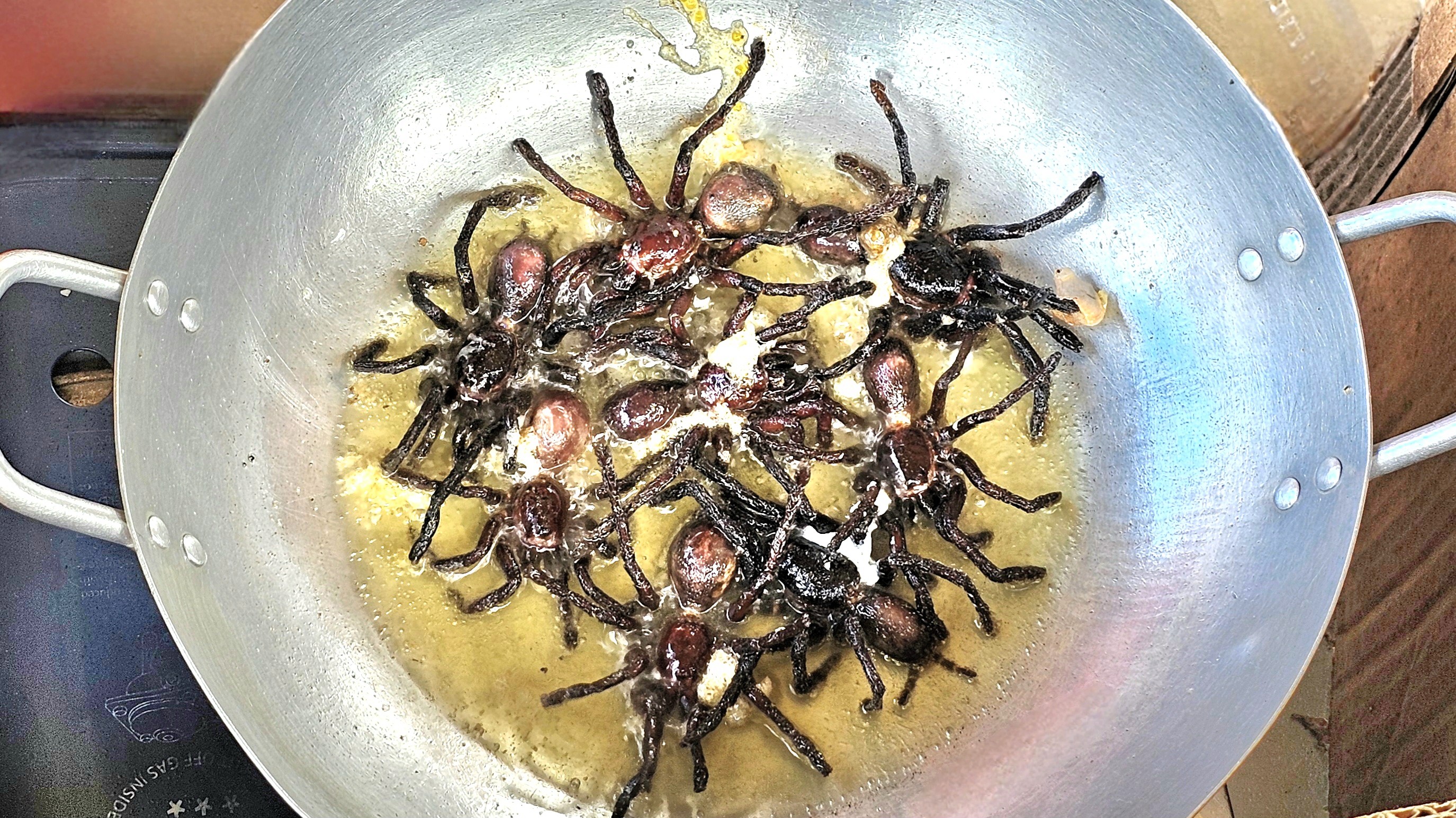 A wok filled with deep-fried tarantulas, sizzling in hot oil, showcasing the preparation of a local delicacy.
