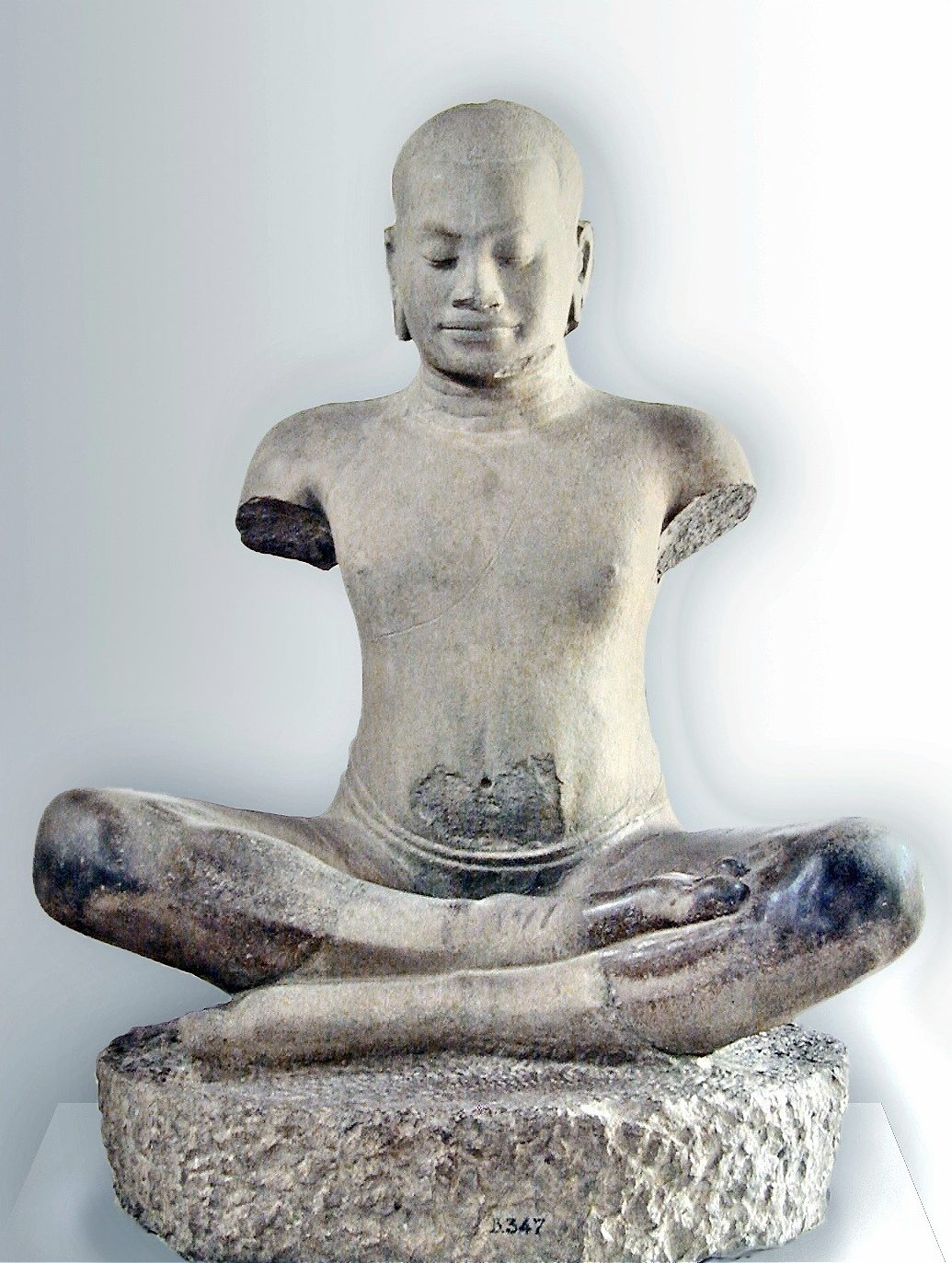 A stone sculpture of a seated figure in a meditative pose, featuring a smooth head and a serene expression, suggesting a representation of Buddha.