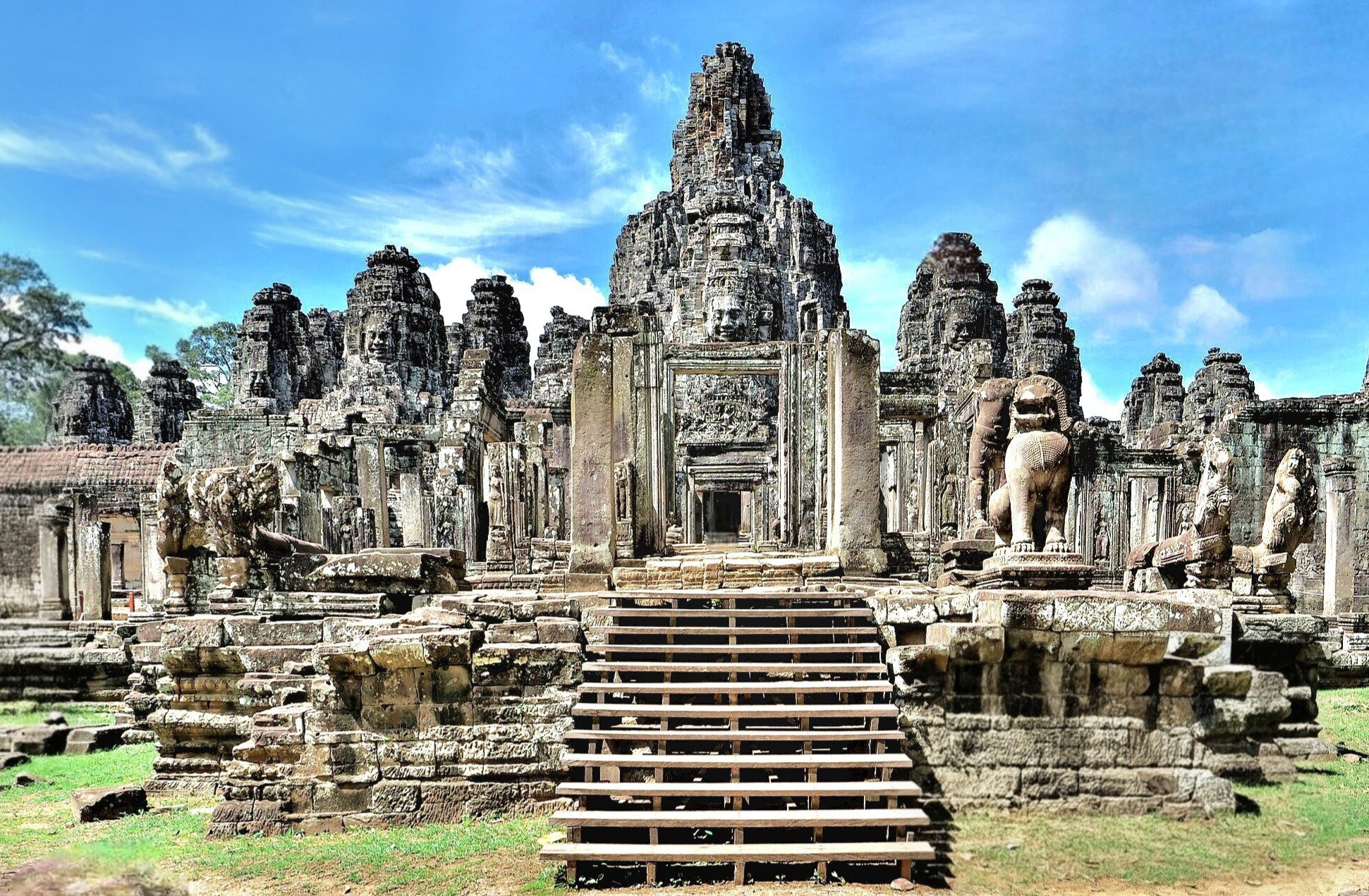 A view of Bayon Temple featuring its iconic stone towers and intricate sculptures, including lion figures, set against a clear blue sky.
