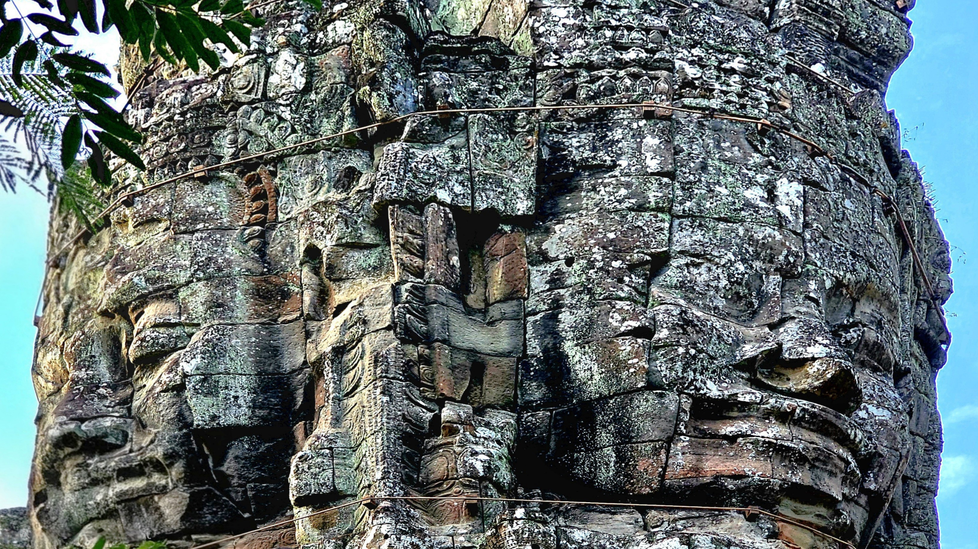 Close-up view of a stone tower at Ta Prohm temple featuring intricate bas-relief carvings and moss-covered surfaces under a clear sky.