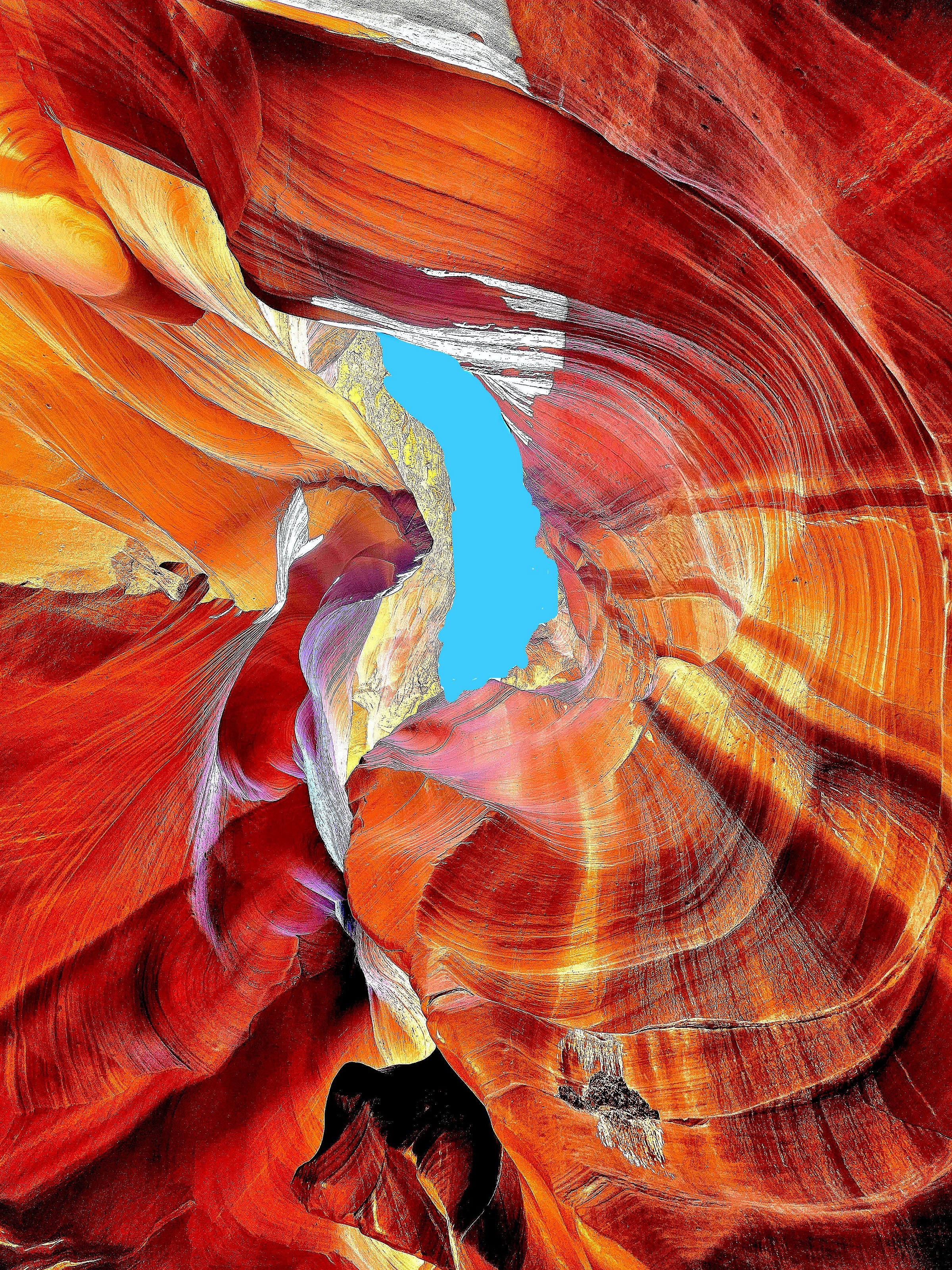 An abstract view of a colorful rock formation in a canyon, featuring vibrant reds, oranges, and hints of blue sky visible through the narrow opening.