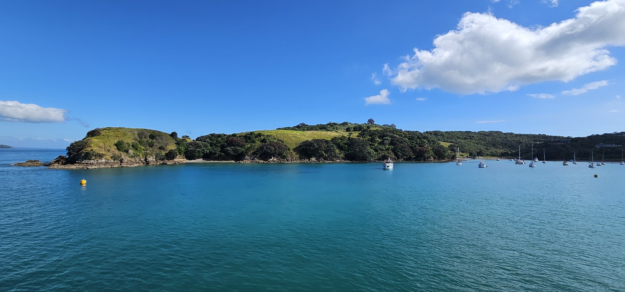 A serene coastal scene featuring a lush green island surrounded by calm turquoise waters, with several boats anchored in the bay under a clear blue sky.