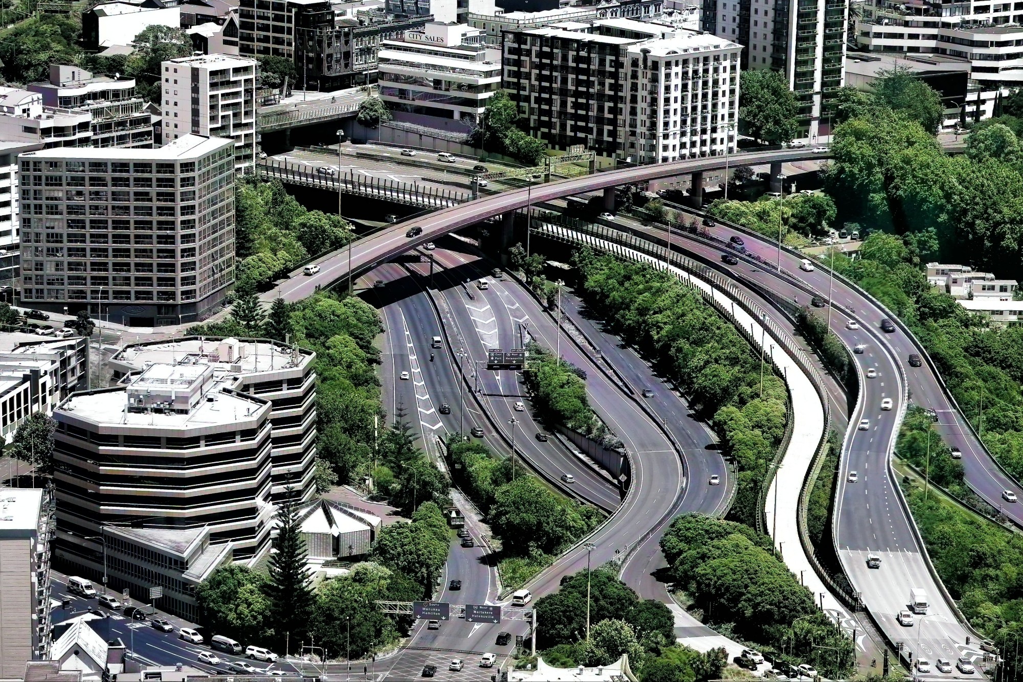 Aerial view of urban roads and highways surrounded by greenery and buildings, showcasing multiple intersections and traffic flow.